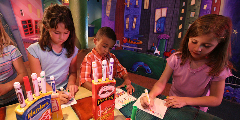 Three kids coloring with markers on a table at Kaleidoscope